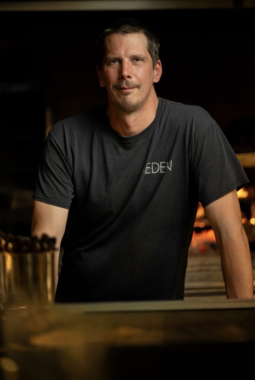 Chef Rich Strub at the pass at Eden, the wood-fired hearth glowing behind him